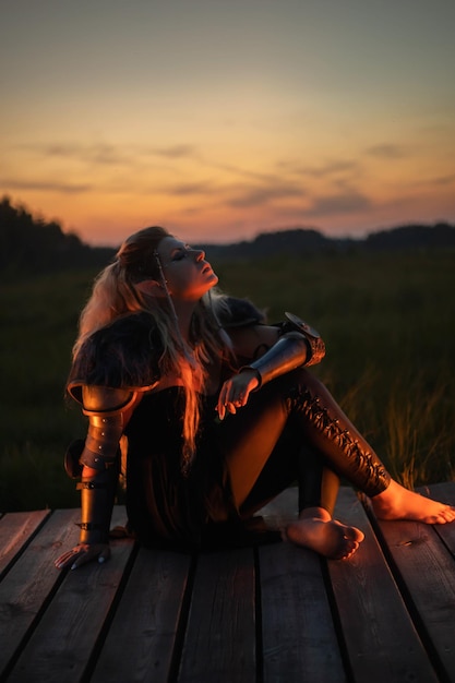 Photo elf girl in armor sits against the backdrop of sunset