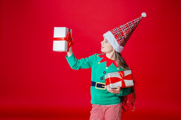 Elf girl with gifts santa claus helper on a bright red bright\
colored background copy space