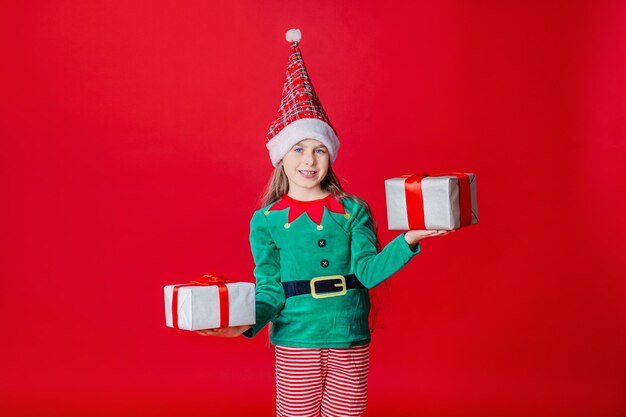 Elf meisje met geschenken Santa Claus helper op een felrode felgekleurde achtergrond Ruimte kopiëren