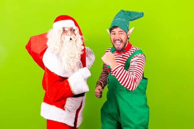 Foto elfo e babbo natale insieme e felici su sfondo verde sorride alla macchina fotografica