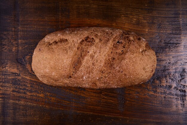 Photo eliptic form bread on a wooden, bread from a stove on dark boards