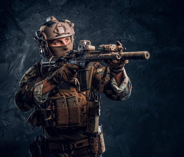 Elite-eenheid, special forces-soldaat in camouflage-uniform met aanvalsgeweer en gericht met optisch zicht. studiofoto tegen een donkere getextureerde muur