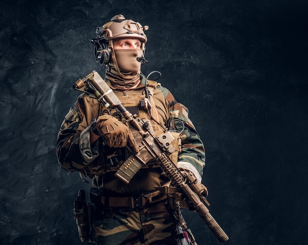 Elite unit, special forces soldier in camouflage uniform posing with assault rifle. Studio photo against a dark textured wall