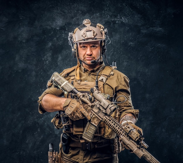 Elite unit, special forces soldier in camouflage uniform posing with assault rifle. Studio photo against a dark textured wall