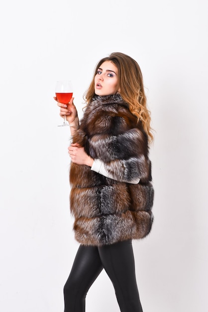 Elite vrije tijd. Lady fashion model krullend kapsel geniet van elite wijn. Wijncultuur concept. Redenen om rode wijn te drinken in de winter. Vrouw drinkt wijn. Meisje mode make-up dragen bontjas houd glas alcohol.