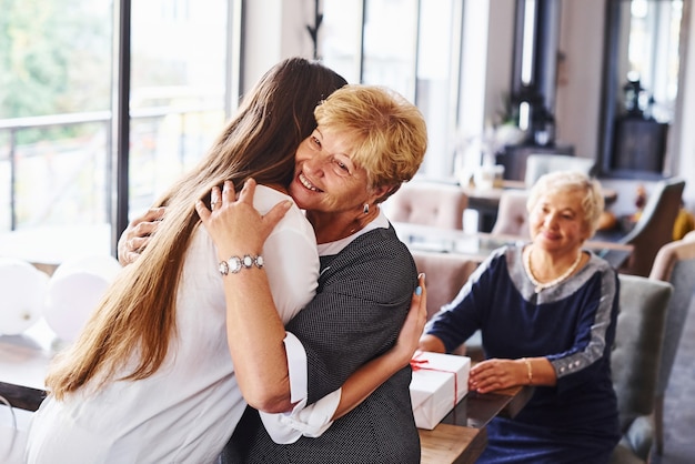 Elkaar omhelzen. Senior vrouw met familie en vrienden die een verjaardag binnenshuis viert.