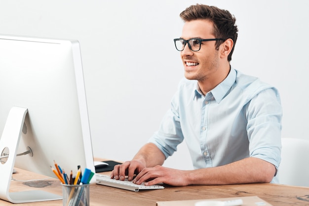 Elke dag een geweldige oplossing. vrolijke jonge knappe man met een bril die op de computer werkt en glimlacht