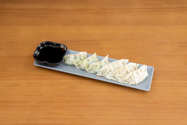 Elongated tray of steamed gyozas stuffed with vegetables with soy sauce for dipping on wooden table