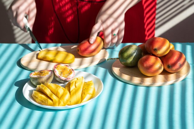 Foto emale le mani tagliano il mango e il frutto della passione, colazione alla frutta