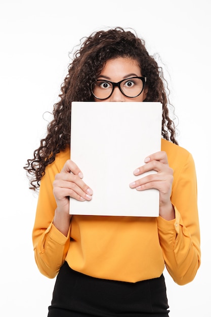 Embarrassed african young businesswoman hiding her face behind blank paper