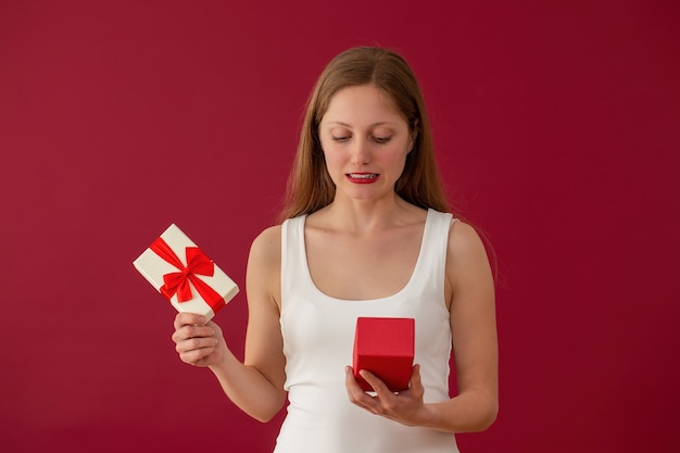 Embarrassed woman looking on a present on red background