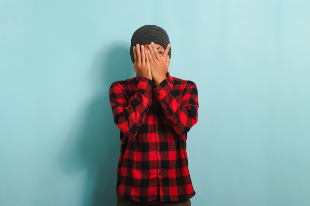 Фото Смущенный молодой азиат закрывает лицо рукой, изолированной на синем фоне
