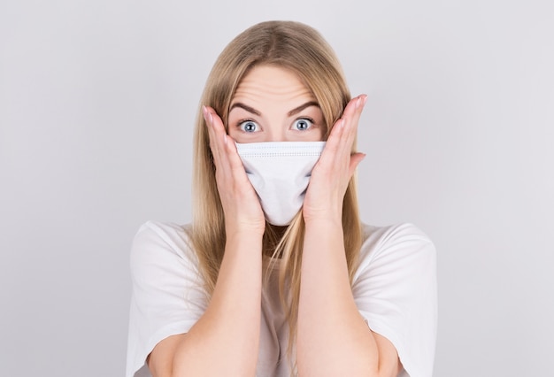 Embarrassed Young caucasian woman wearing medical mask standing over isolated white wall, with shocked expression.