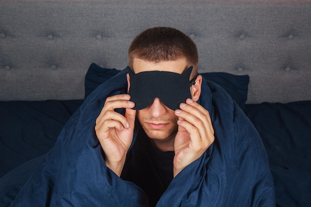 自宅で毛布を着た恥ずかしい若者は、自宅のスタジオポートレートでリラックスしながら睡眠マスクを着用し、気分が良いリラックスしたライフスタイルのコンセプト