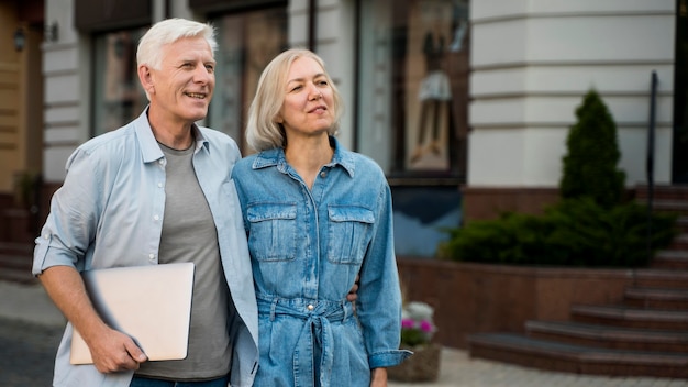 Embraced older couple outdoors in the city with tablet