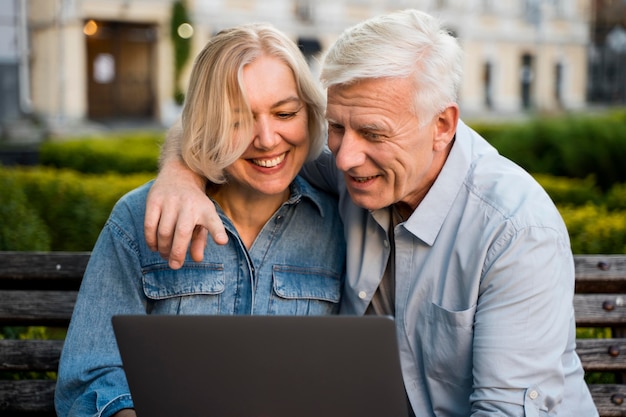 Embraced smiley older couple outdoors with laptop