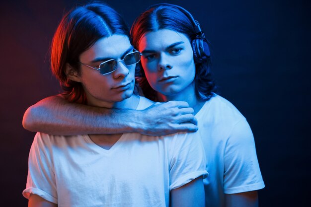 Embracing each other. Portrait of twin brothers. Studio shot in dark studio with neon light