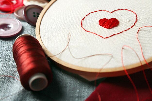 The embroidery hoop with canvas and red sewing threads on table close up