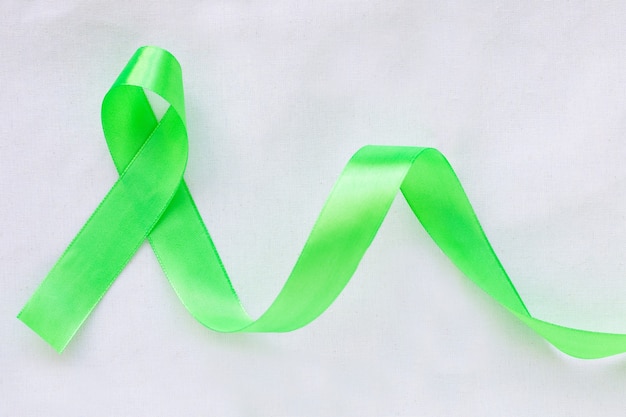 Emerald green or jade green ribbon curl on white fabric\
background with copy space, symbol for liver cancer awareness.