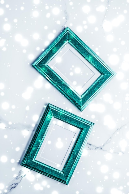Emerald green photo frame and glowing glitter snow on marble flatlay background for Christmas and winter holidays