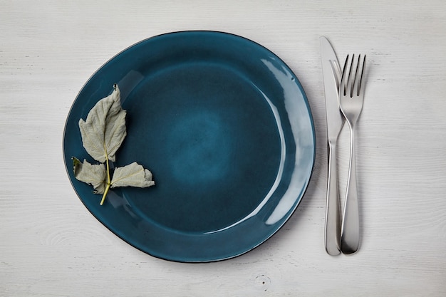 Emerald handmade ceramic plate with cutlery on a white wooden table. Top View Menu