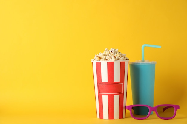 Emmer met popcorn, drank en glazen op gele achtergrond
