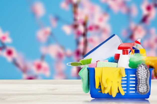 Emmer of mand met schoonmaakartikelen op houten tafel en wazige roze bloemenboomachtergrond.