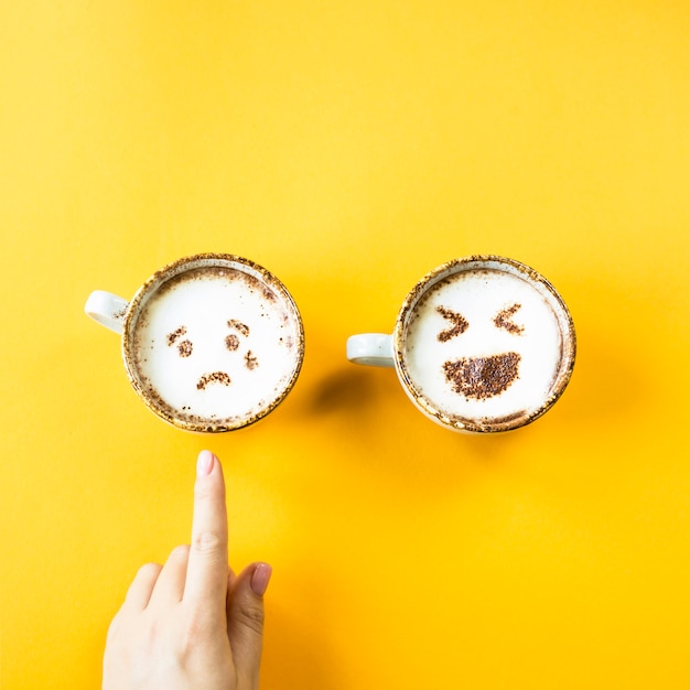 Emoji&#39;s gelach en verdriet worden getekend op cappuccino-kopjes op een gele achtergrond