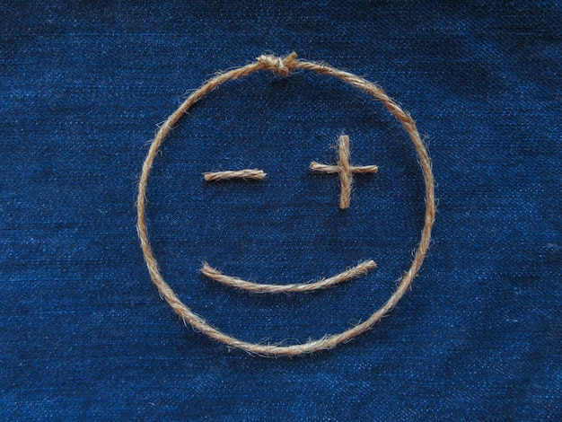 Emoji. Улыбающийся смайлик из шпагата на синей джинсовой ткани. Крупный план