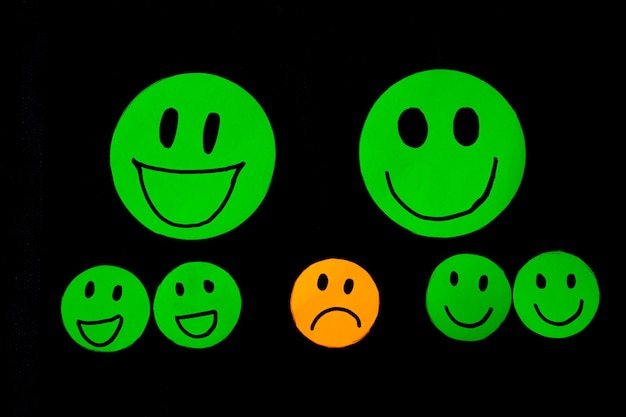 Emoticon icons of papercut smiley faces surrounding a sad face concept of emotions psychology assessment mental health therapy Black background