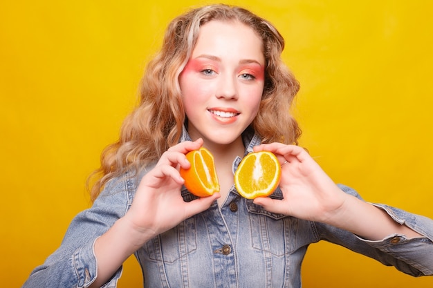 Emoties, gezondheid, mensen, eten en beauty concept - Beauty Model Girl neemt Juicy Oranges. Mooi blij tienermeisje met sproeten, grappig kapsel. gele make-up. Professionele make-up. Sinaasappelschijfje