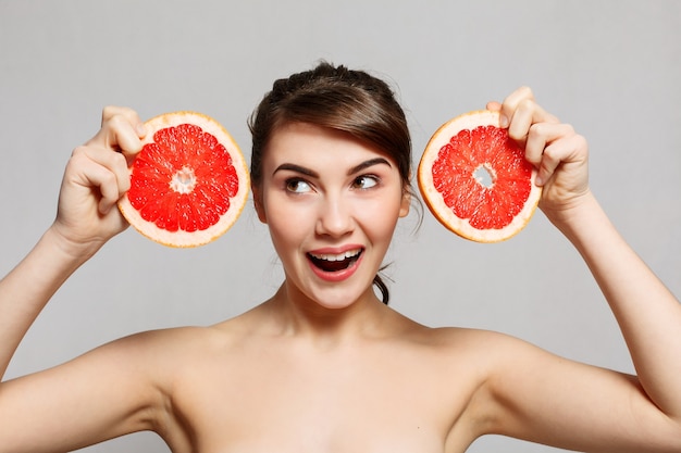 Emoties, gezondheid, mensen, voedsel en schoonheidsconcept - Schoonheidsportret van een gelukkige vrouw met een grapefruit, emotioneel portret. meisje is verrast