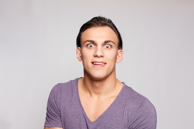 Emotion, advertisement and people concept - Handsome young man on grey background looking at camera. Portrait of laughing young man in pockets leaning against grey wall. guy is surprised