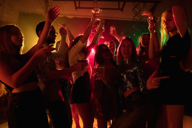 Emotion. A crowd of people in silhouette raises their hands, dancing on dancefloor on neon light background. Night life, club, music, dance, motion, youth. Bright colors and moving girls and boys.