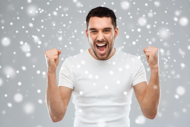 emotion, gesture, winter, christmas and people concept - angry young man holding fists over snow on gray background