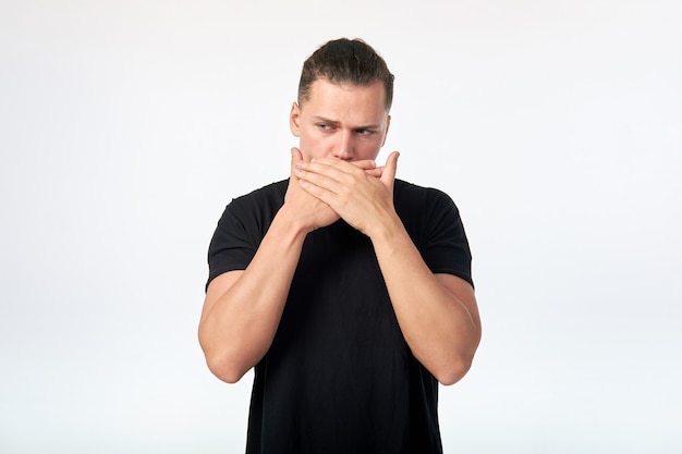 Emotion. Portrait of young scared man covering his mouth with hands.