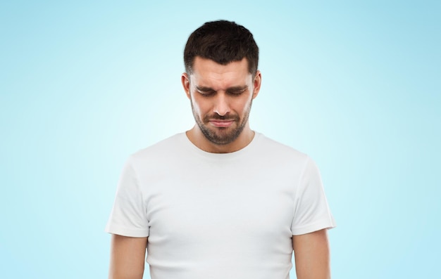 emotion, sadness and people concept - unhappy young man over blue background