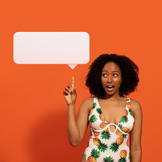 Photo emotional african woman in swimwear pointing at speech balloon