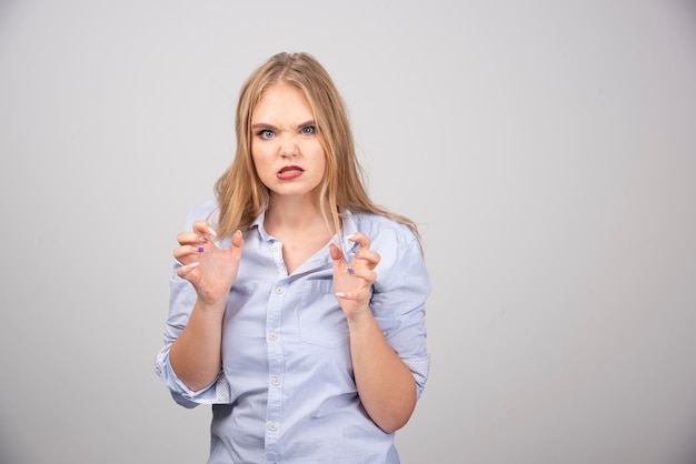 Emotional angry woman standing and looking against gray wall .