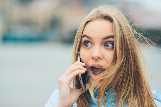 Emotional beautiful blonde talking on the phone outdoors. Female Corrupt faces and indulges in chatting with friends on the cell.