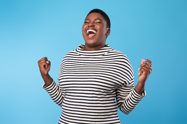 Photo emotional black woman shouting gesturing yes in joy blue background