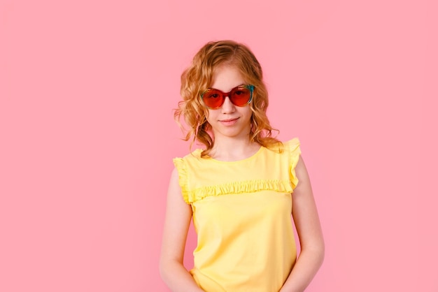 Emotional blonde teen girl in sparkle sunglasses and yellow tshirt laughing to camera on pink background space for text