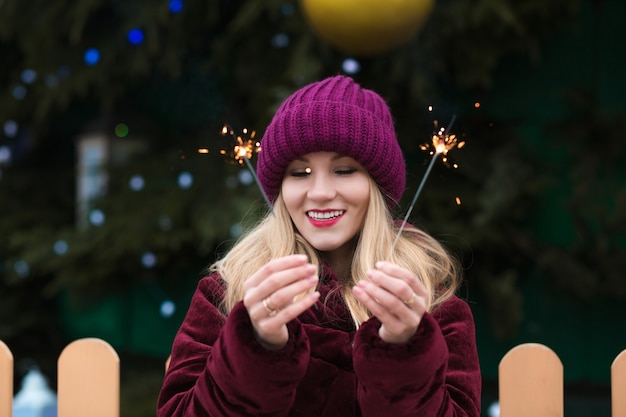 Donna bionda emotiva che si diverte con le scintillanti luci del bengala all'abete rosso di capodanno a kiev