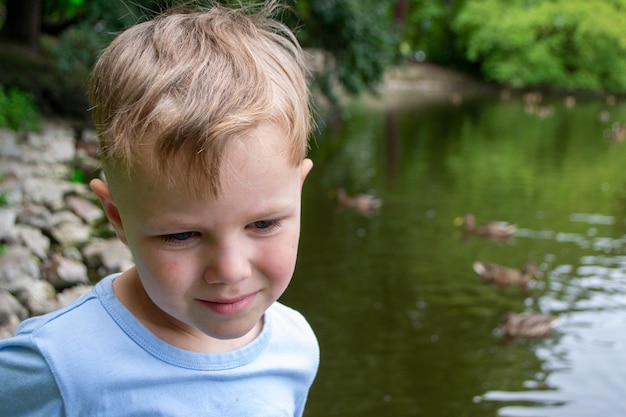 Emotional boy with blond hair hairstyle braids in a green or blue shirt play in the park