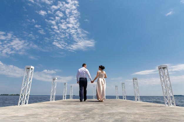 emotional bride and groom walking on the bridge in sunny day .wedding day. man and woman gentle look each other and holding hands outdoors. romantic moment on the date