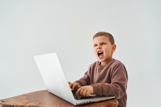 Emotional child with laptop shout Gambling addiction Handsome child gamer play online games on laptop on white background