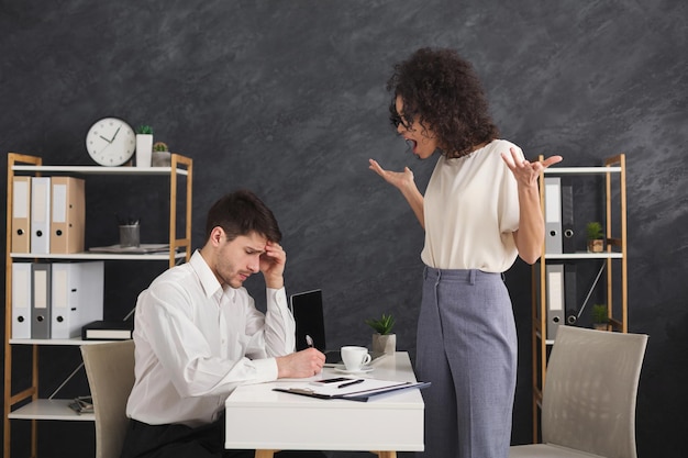 현대 사무실에서 말다툼을 하는 감정적인 젊은 동료 부부. 슬픈 남자 조수에게 소리치는 아프리카계 미국인 비즈니스 여성, 복사 공간, 측면 보기