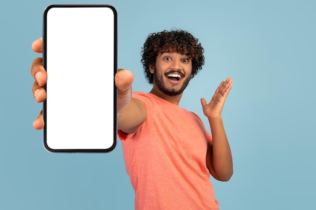Emotional curly indian man showing cell phone with empty screen