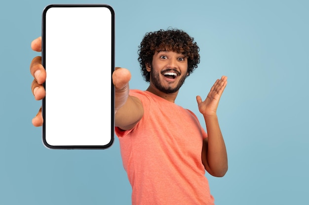 Эмоциональный кудрявый индиец показывает мобильный телефон с пустым экраном