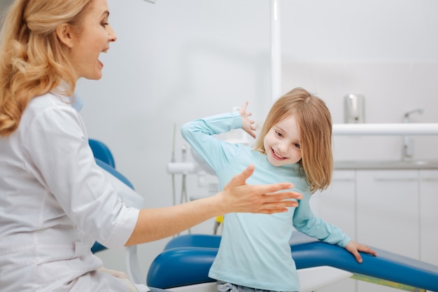 Emotivo carino dentista prominente che dà il cinque al suo piccolo paziente dopo aver estratto il suo dente